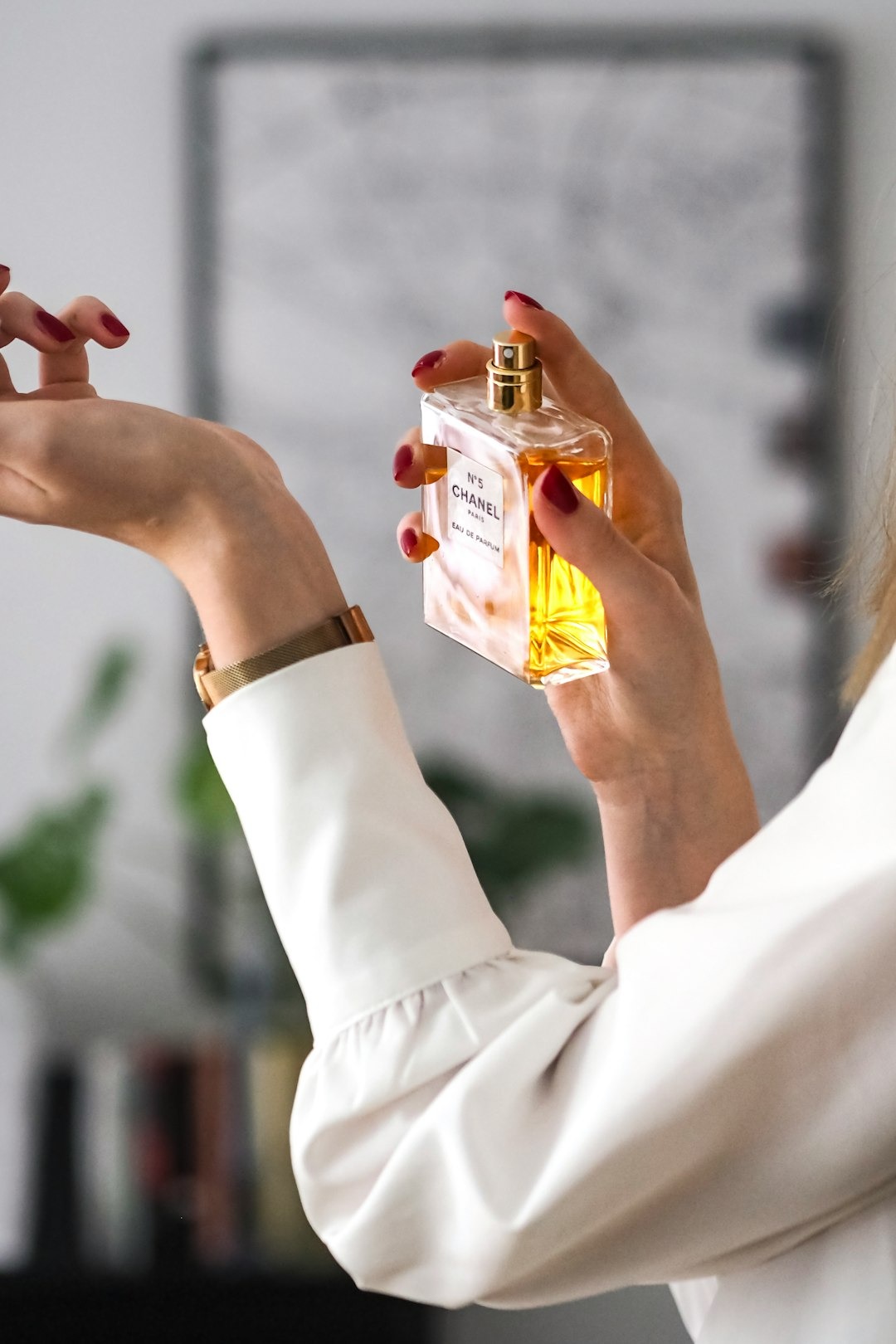 Person with red nails applies perfume to wrist.